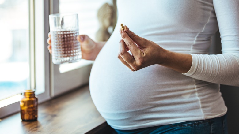 pregnant person holding supplement and water