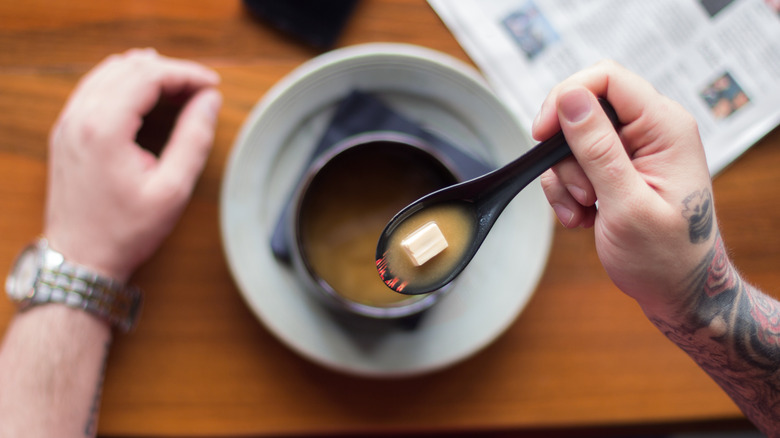 A man holding a spoonful of soup containing a tofu cube