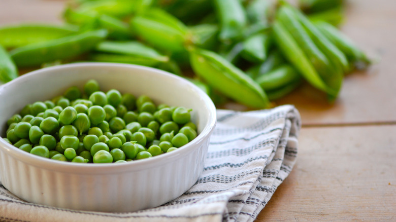 A dish of green peas with their pods in the background