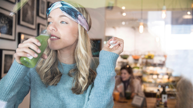 woman drinking light green juice from bottle in shop