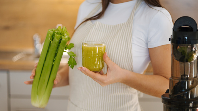 woman in apron holding celery stalk and fresh juice