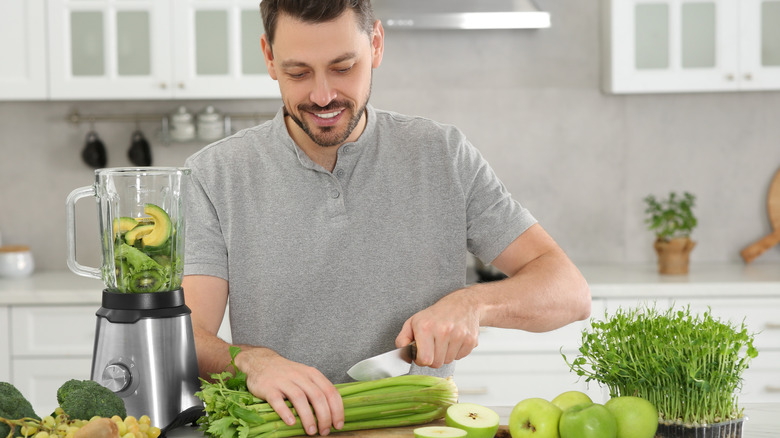 man in kitchen cutting celery to put in blender