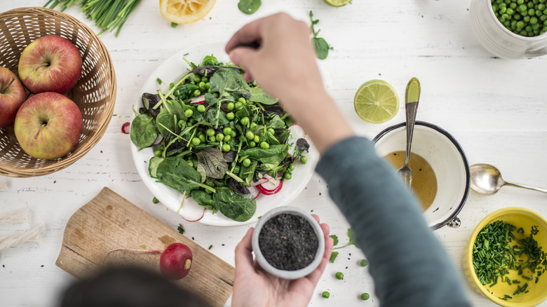 A hand adding seasonings to a pea and greens dish