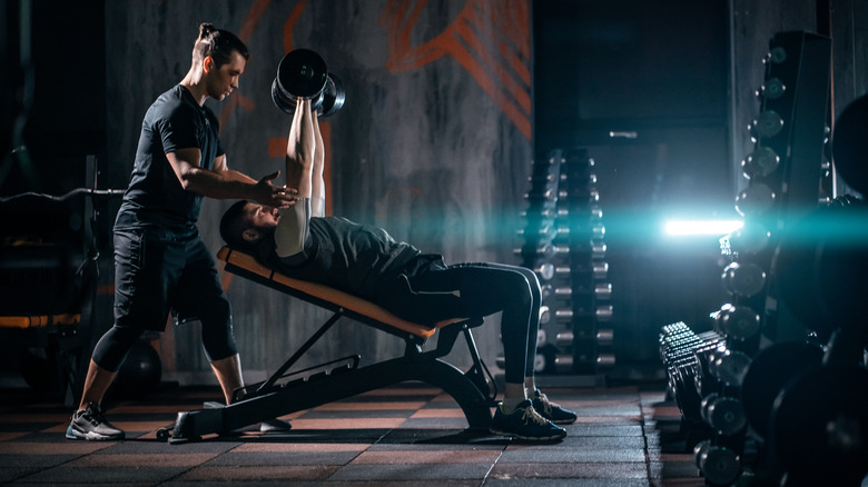 man bench pressing dumbbells on incline bench with spotter in gym