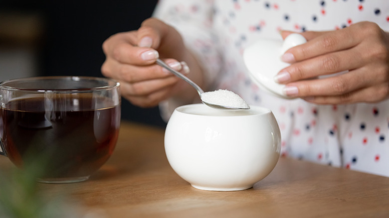 Person spooning sugar into tea