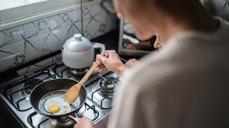 over the shoulder shot of a woman frying an egg