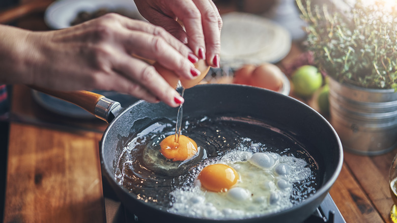 woman's hands cracking eggs over a skillet