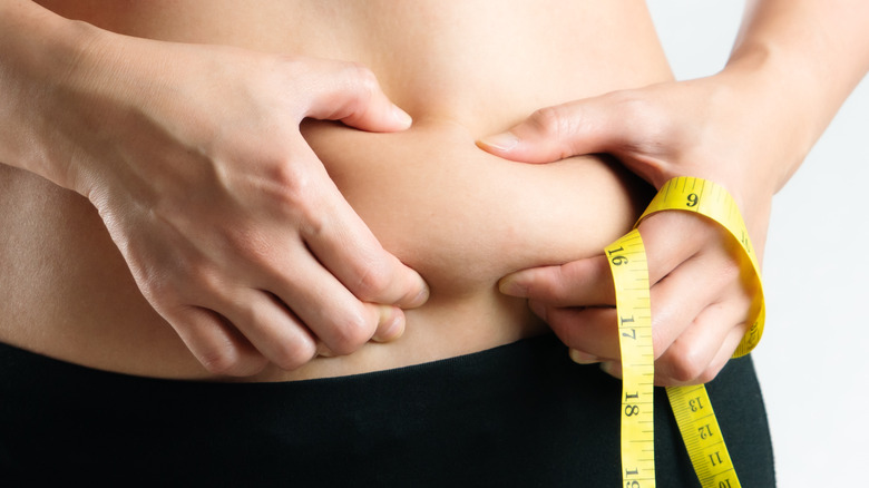 woman pinching belly fat holding a tape measure