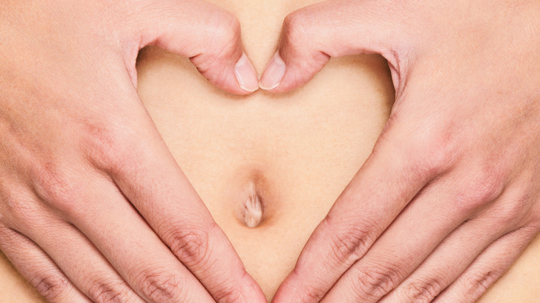 person holding their hands in heart shape around belly button