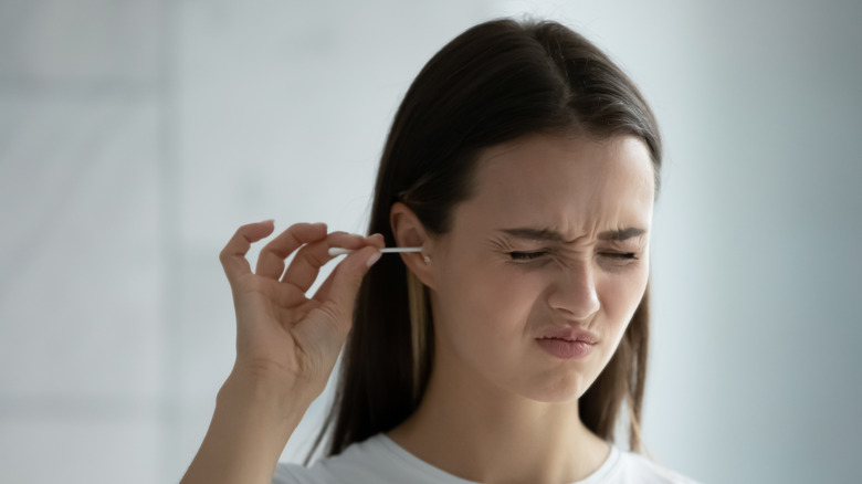 woman wincing cleaning ear with q-tip