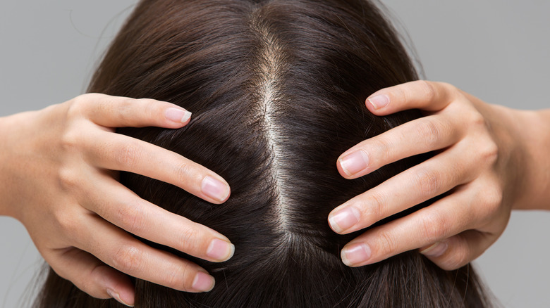 closeup of a woman parting her hair to see scalp