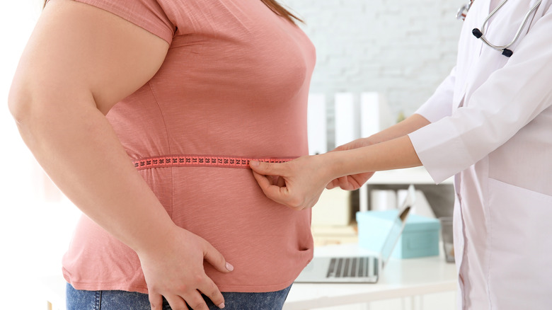 doctor measuring woman's waistline with tape