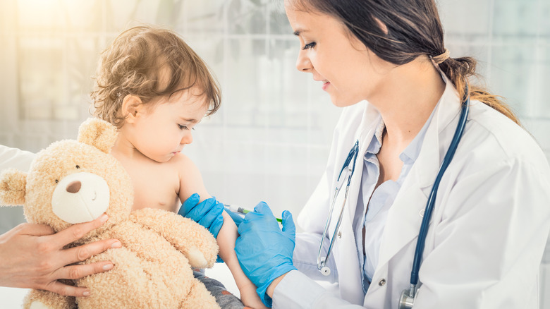 Young child holding a teddy bear receiving vaccine from doctor