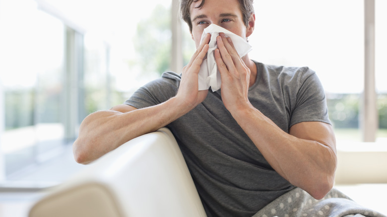 man blowing nose into tissue