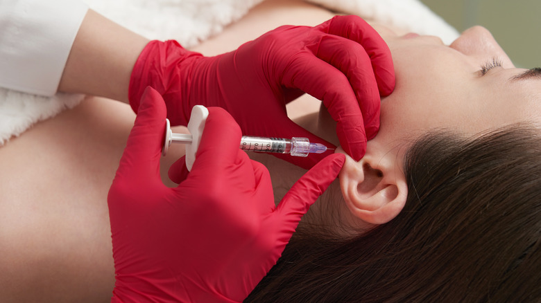 Gloved hands holding syringe injecting earlobe of patient