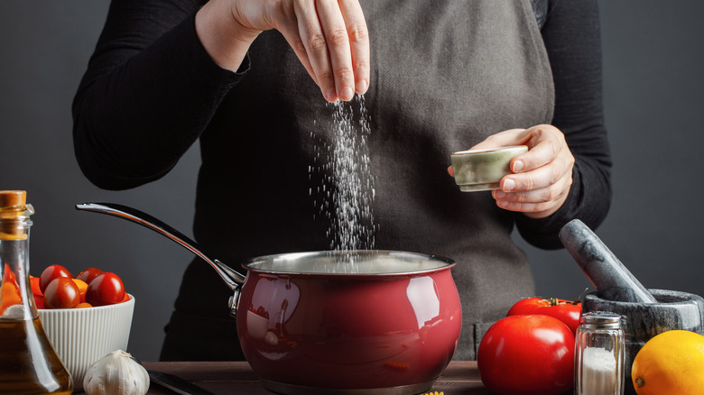 woman adding salt to sauce