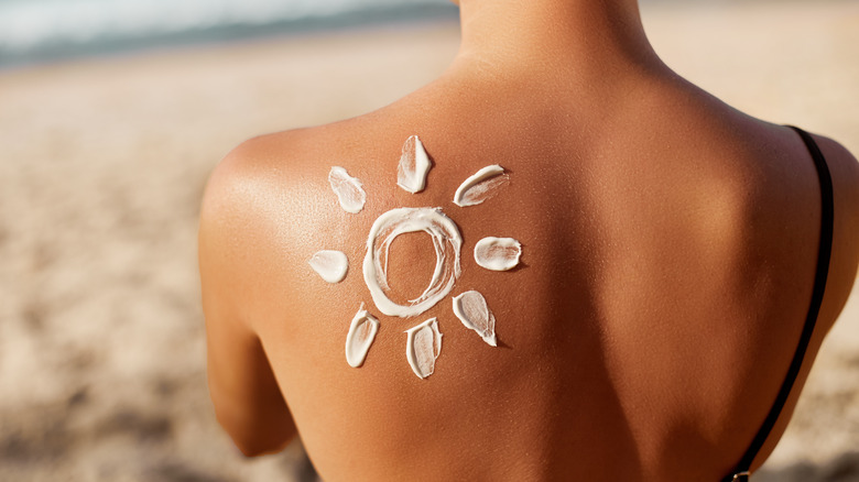 Woman's back with a sun made out of sunscreen on her shoulder