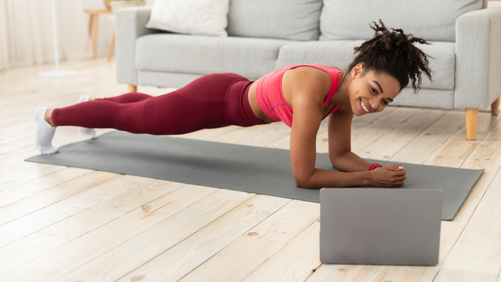 Woman doing plank exercise at home with laptop 