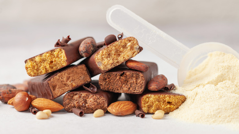 Unwrapped protein bars stacked together beside a scoop of protein powder