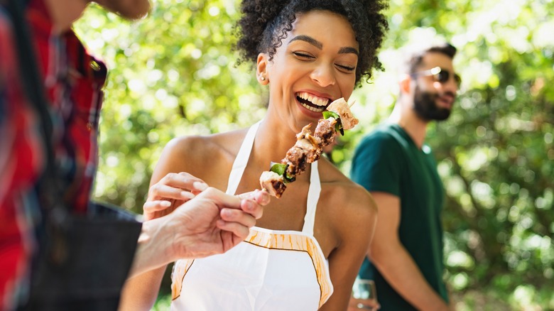 woman laughing as she is about to eat meat skewer