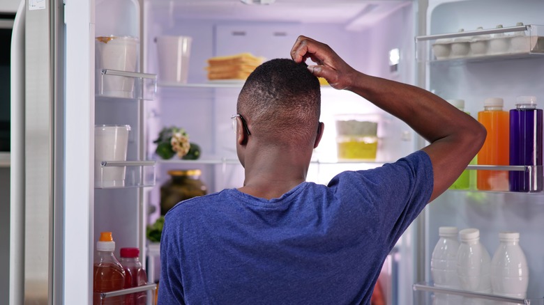 man scratching head trying to find something to eat in fridge