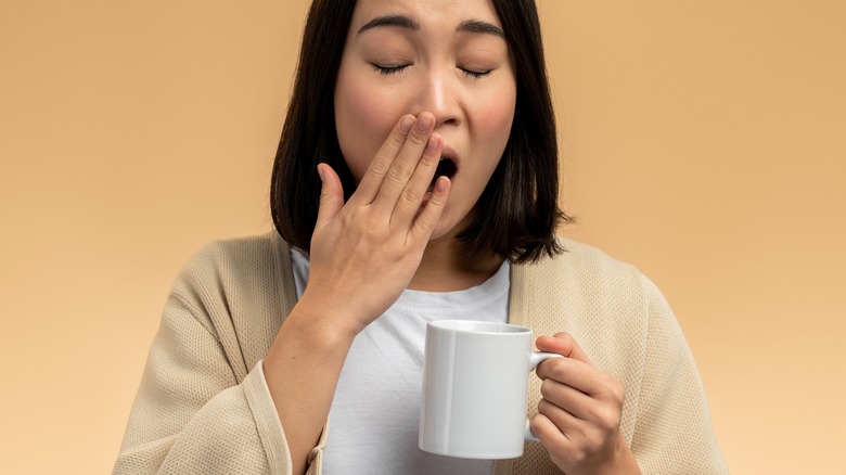 woman yawning holding cup of coffee