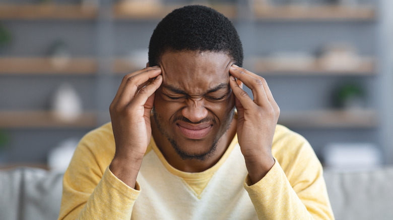 Black man with his hands on his head, dealing with the pain of a headache