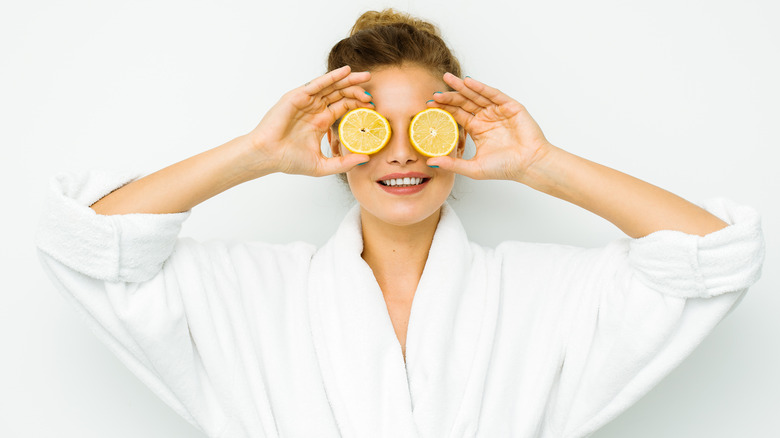 woman holding lemon slices over eyes