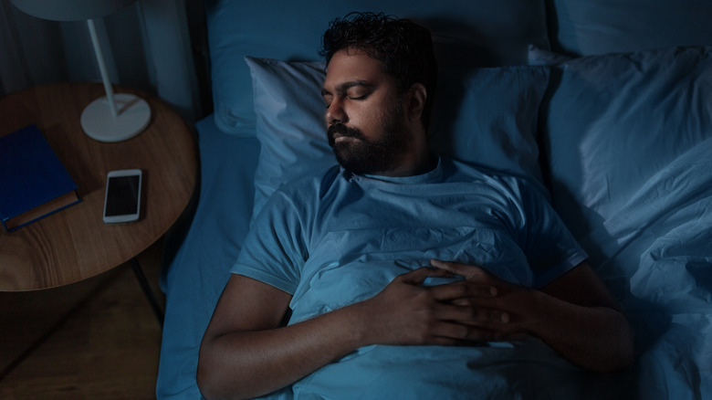 Man asleep next to his phone on bedside table