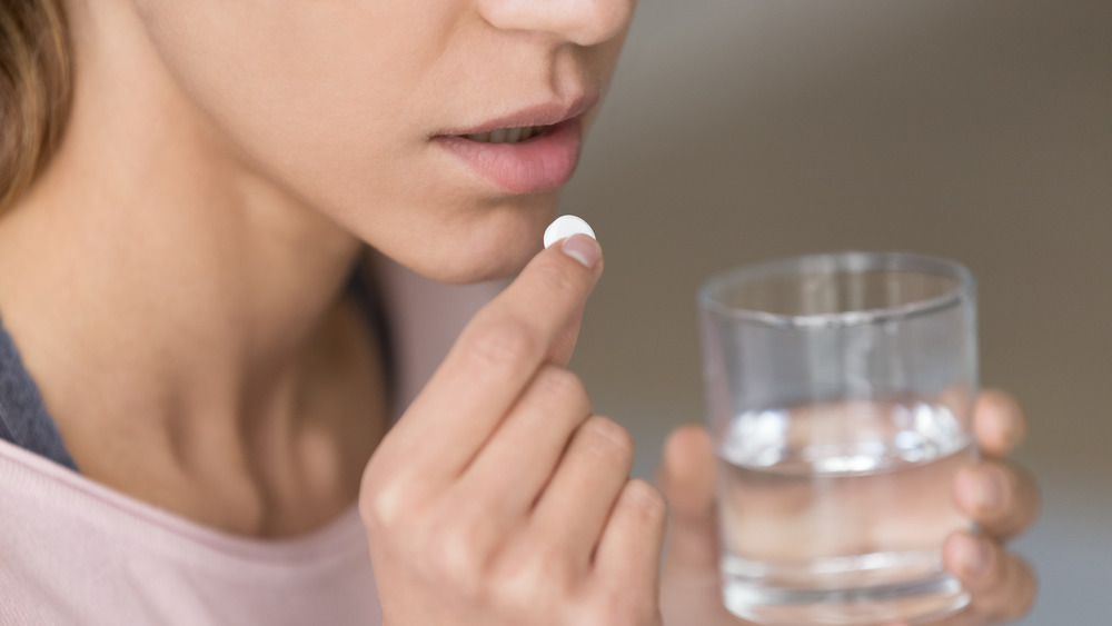 Close up of a woman taking a pill with glass of water