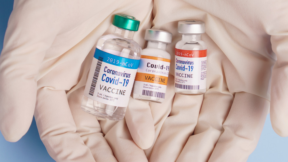 Gloved hands holding vials of three different vaccines