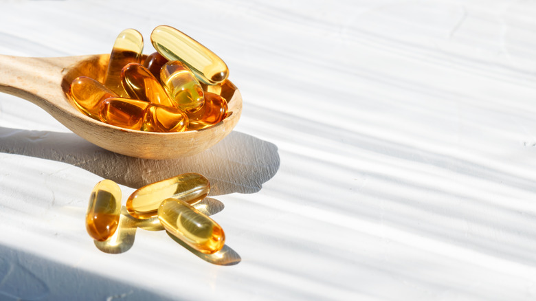 Fish oil capsules sit in a wooden spoon on a white table