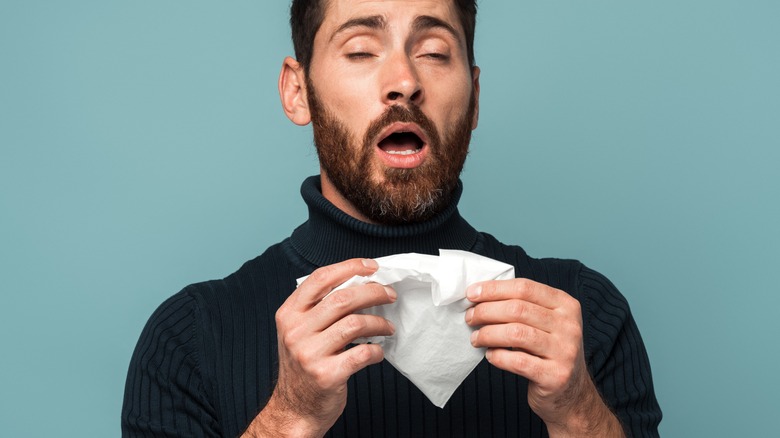 man sneezing and holding tissue