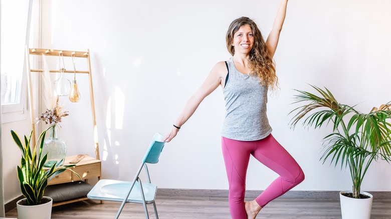 woman doing tree pose while holding onto a chair