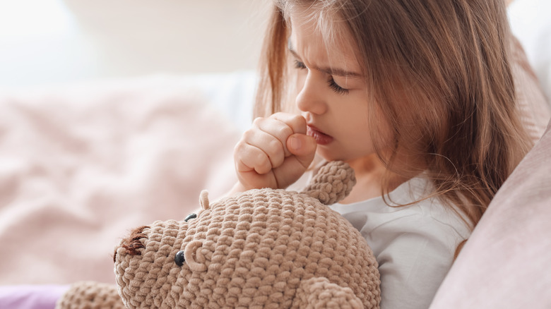 child coughing in bed with toy