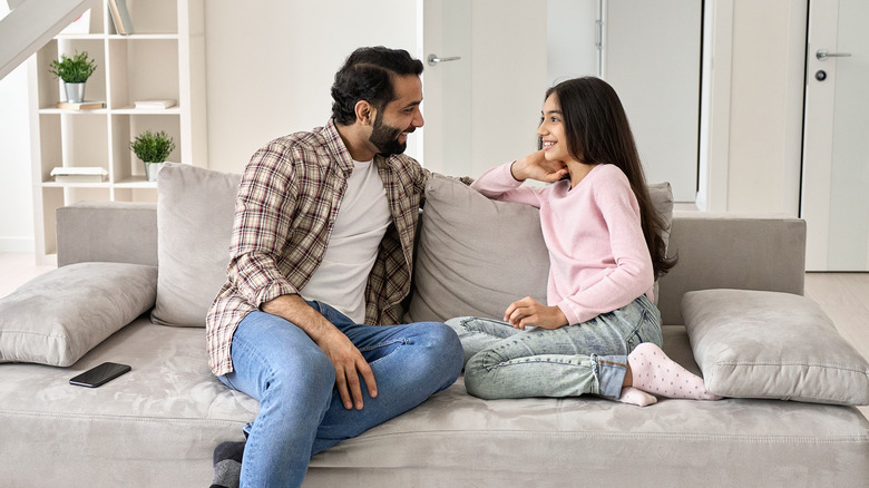 Father and daughter sit on couch talking