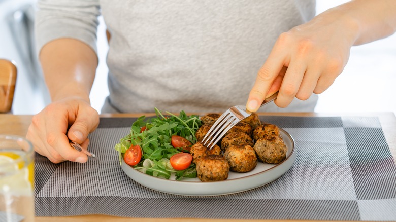 man's hands dipping fork into veggie meatballs and salad