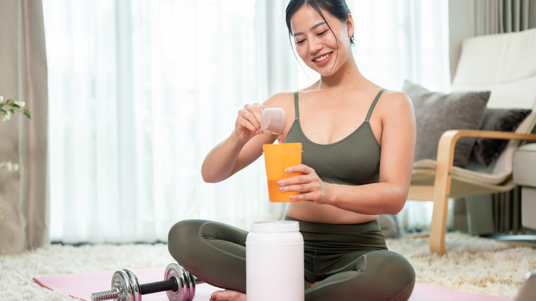 young woman on yoga mat scooping protein powder