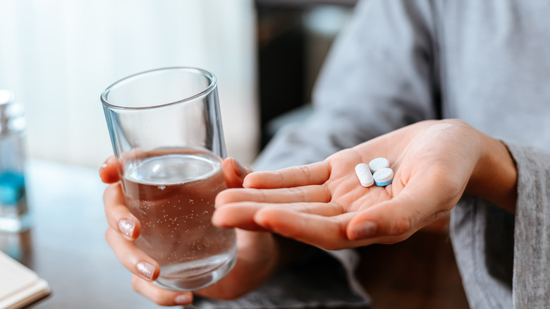close up of hands holding pills and water glass