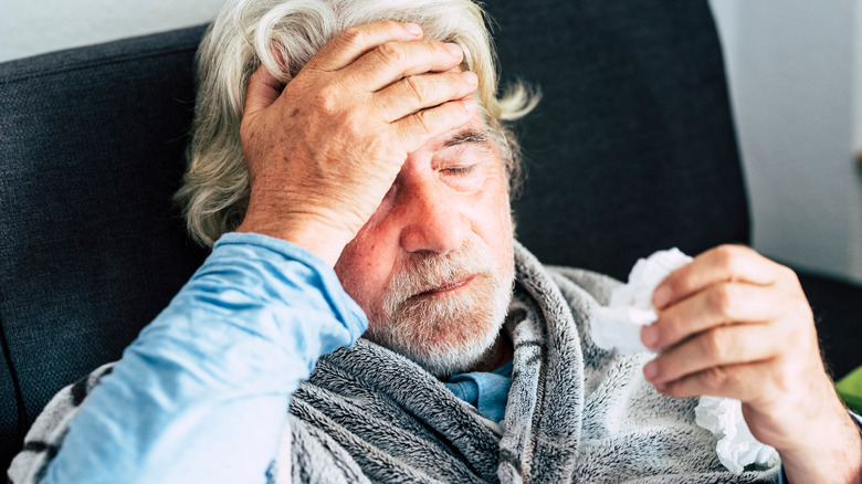 Older man holding his head with one hand and tissue with another