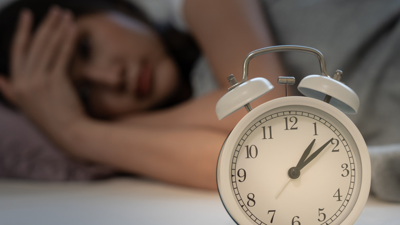 A clock with a wide-awake woman in bed in the background