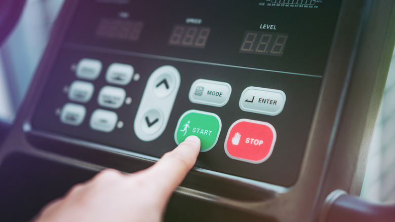 Hand pressing start button on treadmill control panel