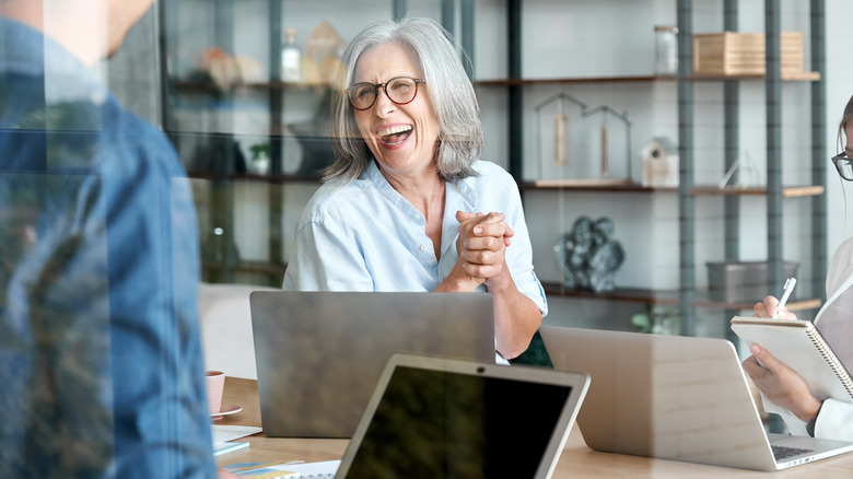 older woman laughing as she sits in front of laptop