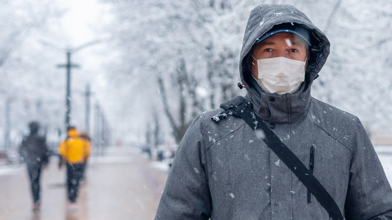 Man in winter jacket and face mask walking covered in snowflakes