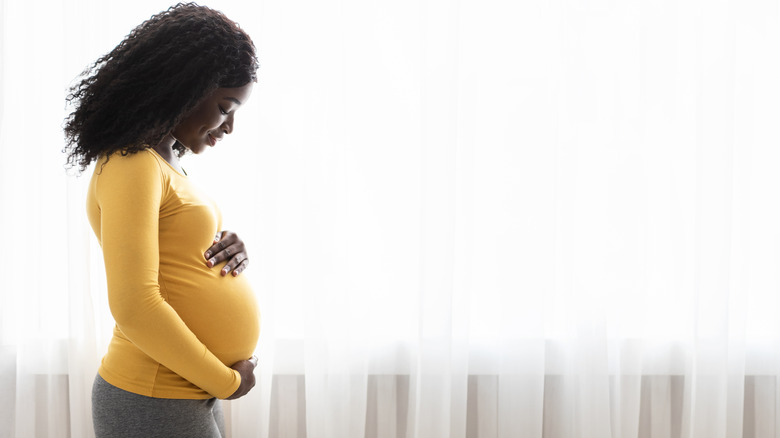 Pregnant black woman hugging her tummy, enjoying her pregnancy