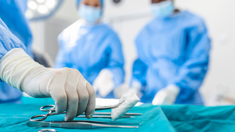 Nurse hand taking surgical instrument for surgeons operating patient in surgical theatre