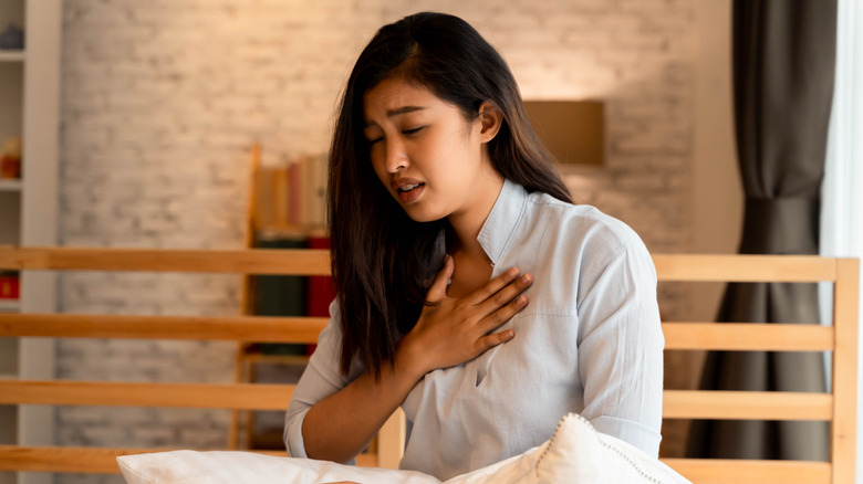 Woman sitting in bed with hand on her chest having trouble breathing