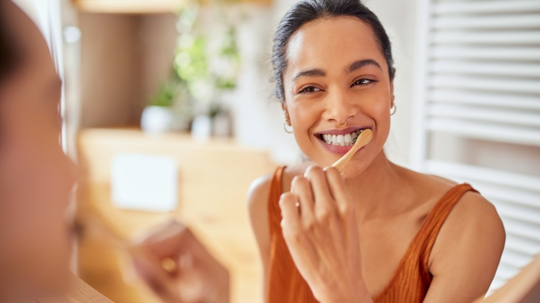 woman brushing teeth in mirror