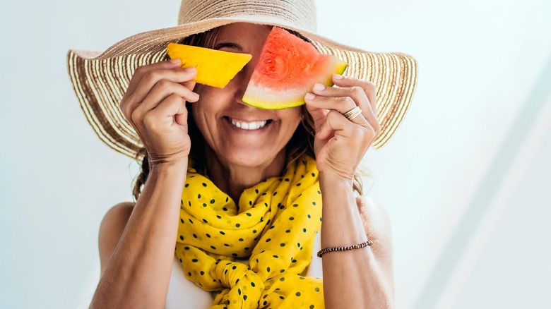 Smiling woman covering eyes with fruit