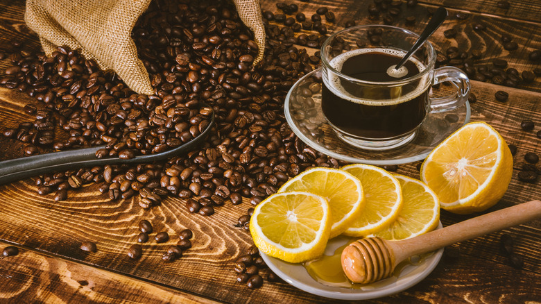 Coffee beans and lemon slices next to cup of coffee